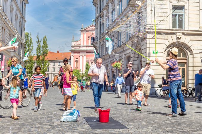 Ljudje na Stritarjevi ulici občudujejo osebo, ki dela milne mehurčke.